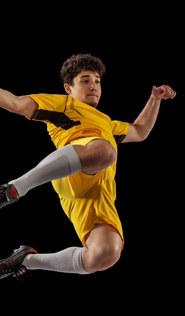 Мужчина футболист отбивает мяч на черном фоне