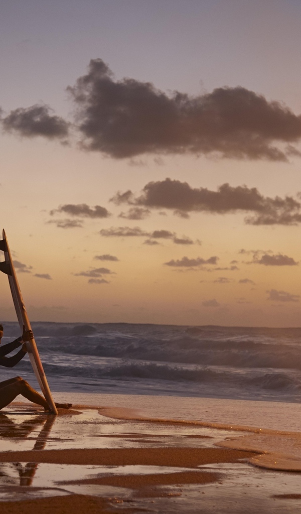 Девушка серфингистка сидит на берегу моря