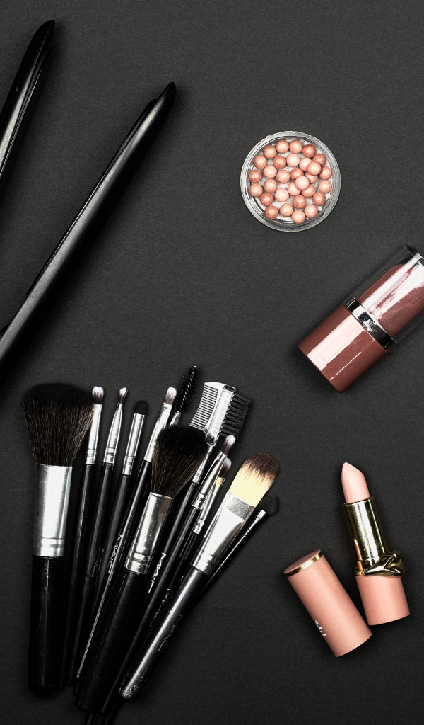 Кисточки с косметикой и плойкой на черном фоне