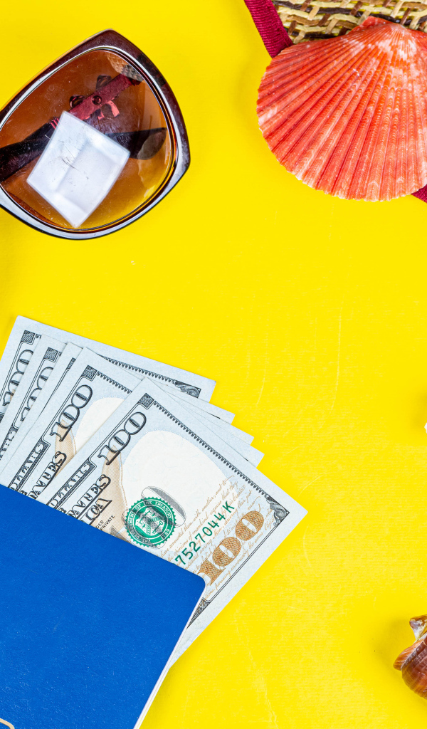 Очки, доллары с паспортом и ракушки на желтом фоне