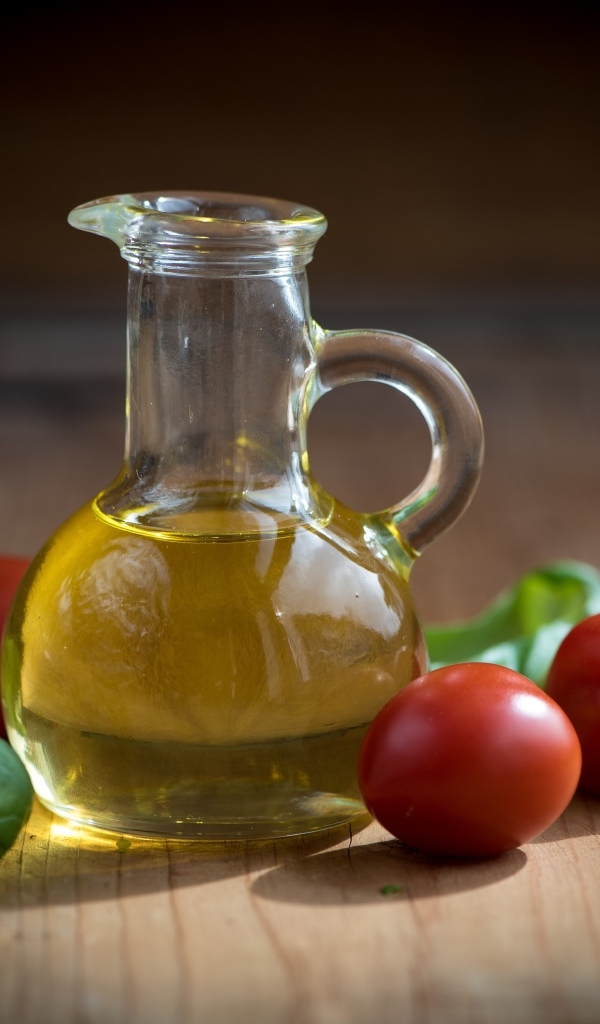 Оливковое масло на столе с базиликом и помидорами