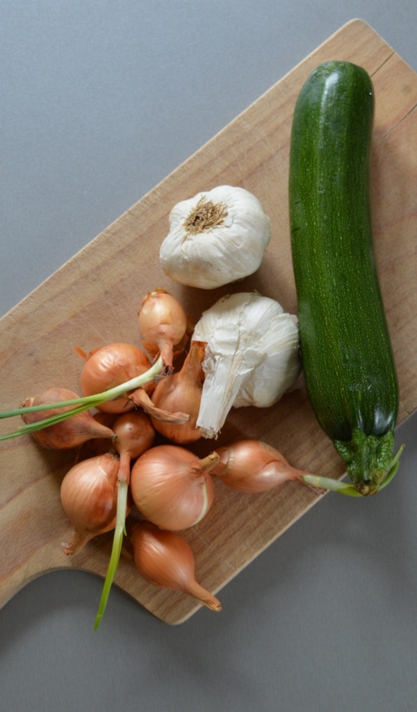 Лук, чеснок и кабачок на разделочной доске с ножом