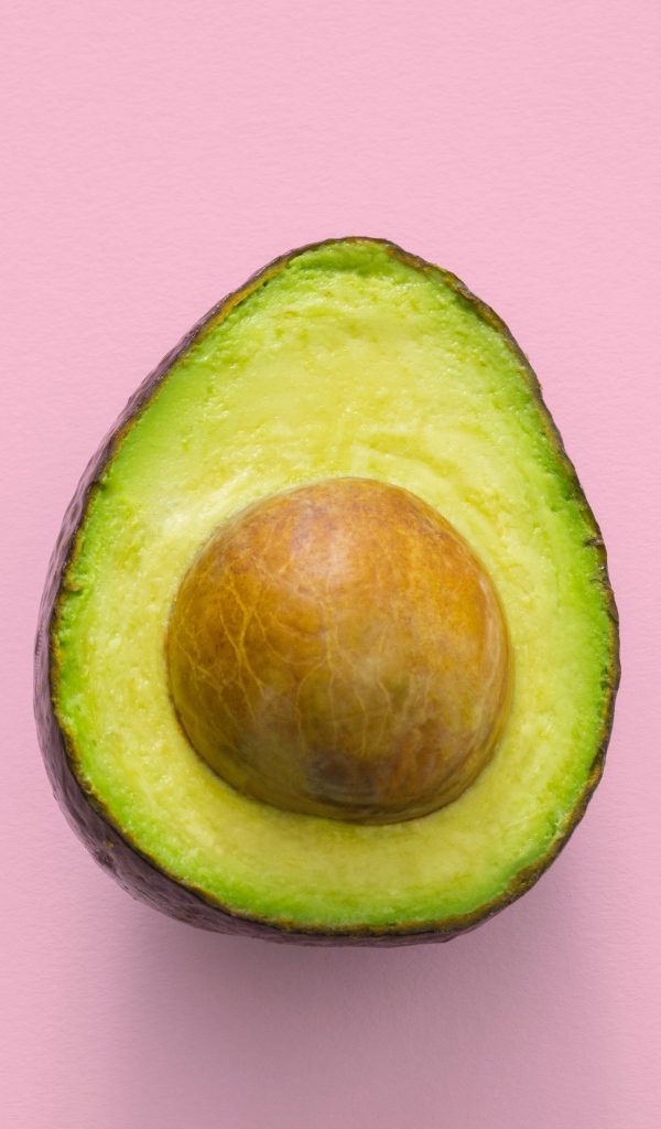 Половина авокадо с большой косточкой на розовом фоне