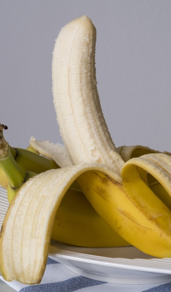 Очищенный банан на тарелке на сером фоне