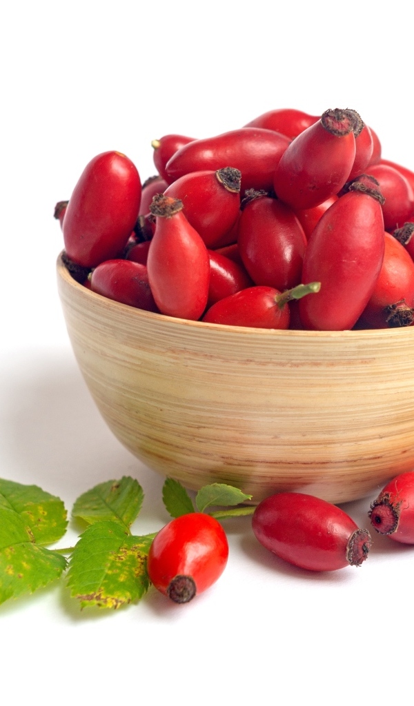 Тарелка с красными плодами шиповника на белом фоне