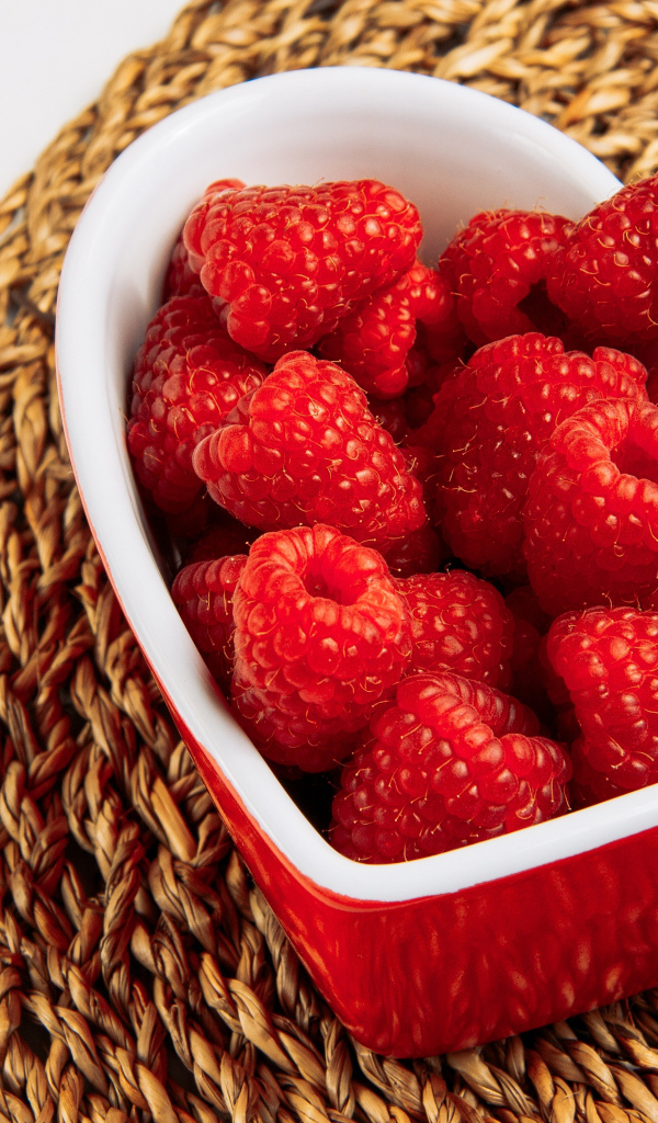 Малина в тарелке в виде сердца на столе