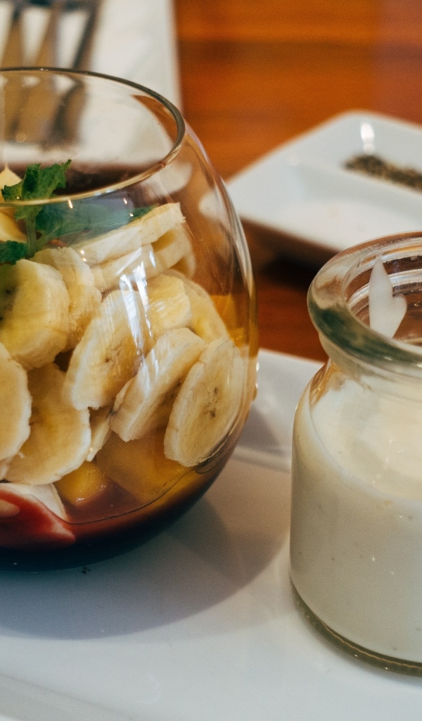 Нарезанные бананы в стакане на столе с йогуртом