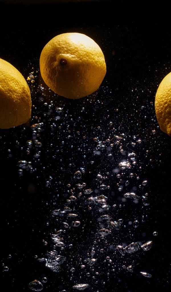 Три желтых лимона с пузырями в воде на черном фоне