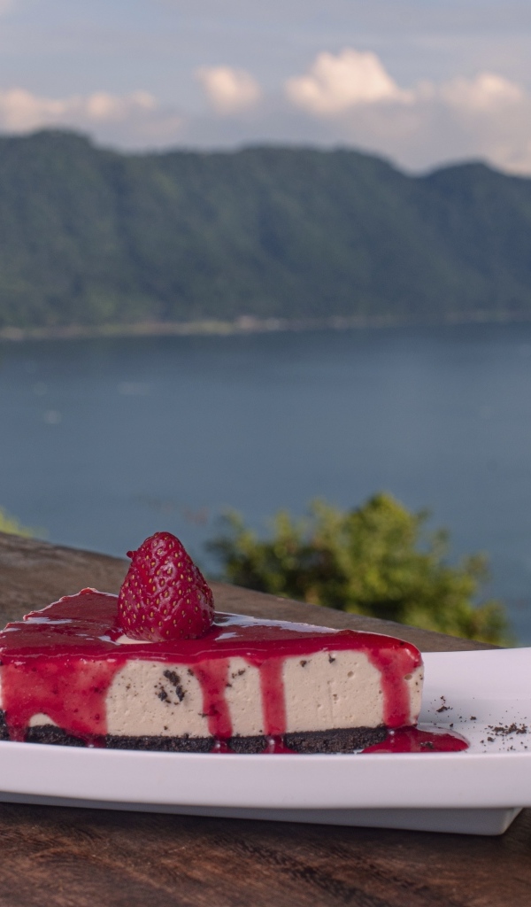 Кусок чизкейка с клубничным джемом на фоне моря
