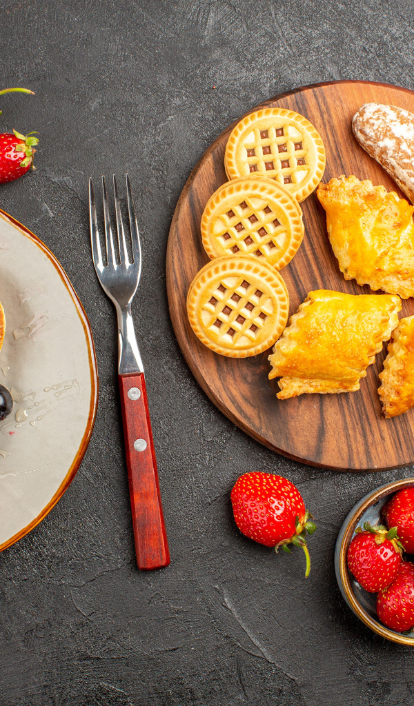 Печенье и оладьи на столе с ягодами клубники и виноградом