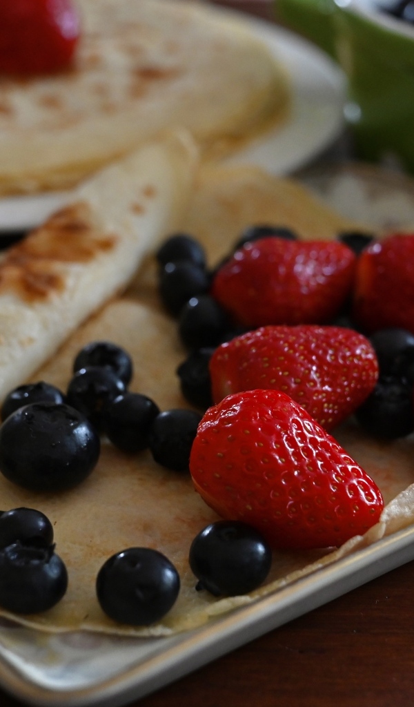 Блин с ягодами черники и клубники на тарелке