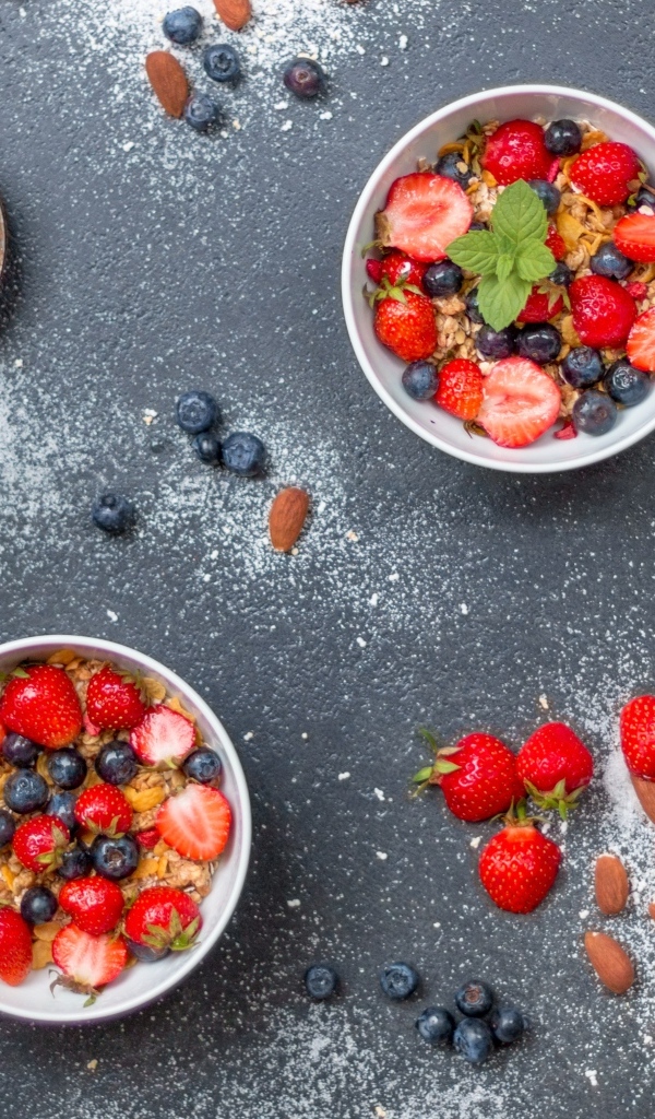 Тарелки с мюсли и ягодами на сером столе с пудрой