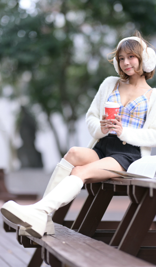 Девушка азиатка с кофе сидит на столе в парке