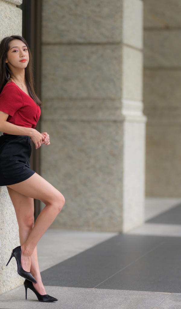 Азиатка в короткой черной юбке стоит у стены