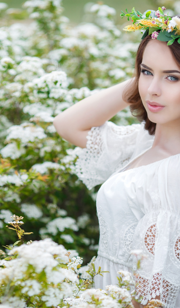 Красивая девушка в белом платье с венком на голове в белых цветах