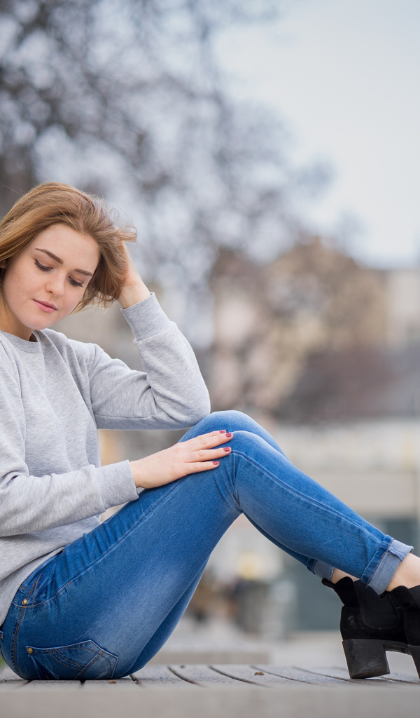Милая девушка в синих джинсах сидит на лавке