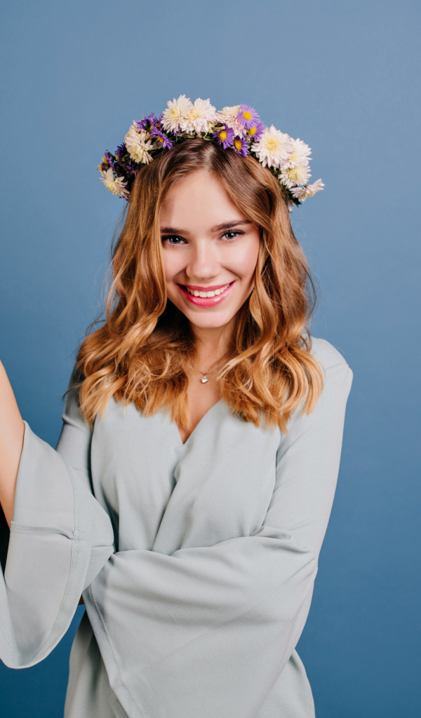 Милая улыбающаяся девушка с венком на голове на сером фоне