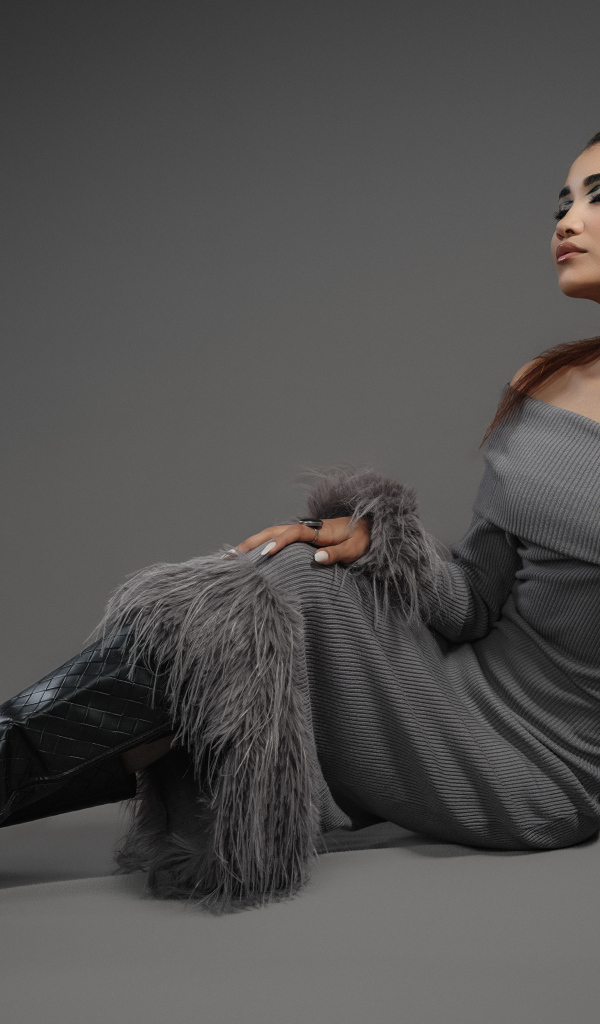 Девушка в платье и длинных черных сапогах на сером фоне