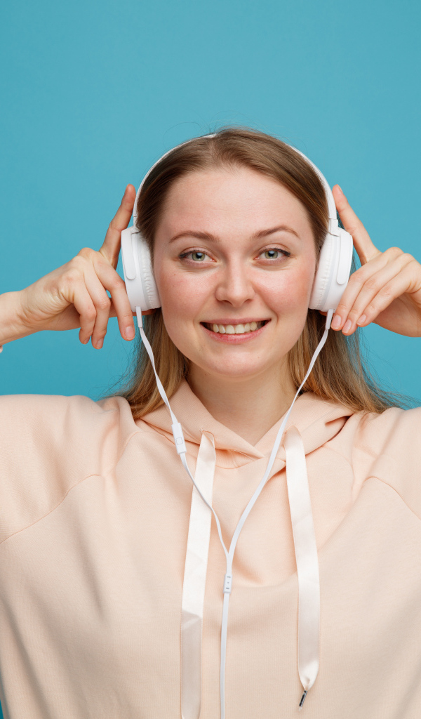 Улыбающаяся девушка в наушниках на голубом фоне