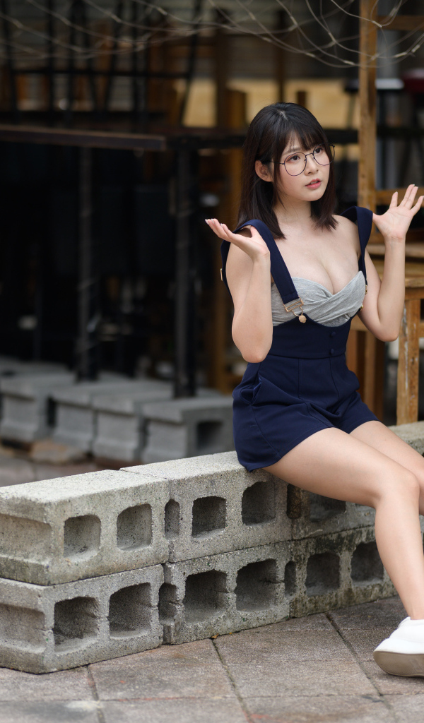 Молодая азиатка в очках сидит на шлакоблоке