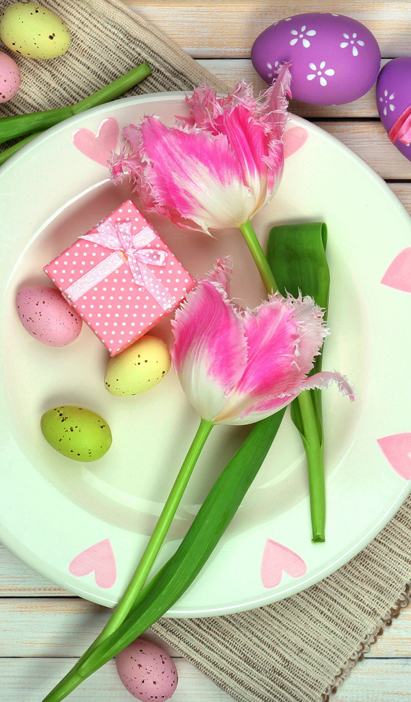 Пасхальные яйца с тюльпанами на тарелке на столе