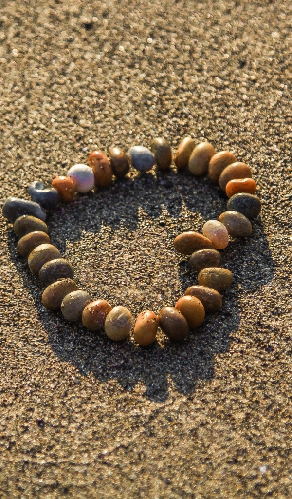 Сердце из камней на морском песке летом