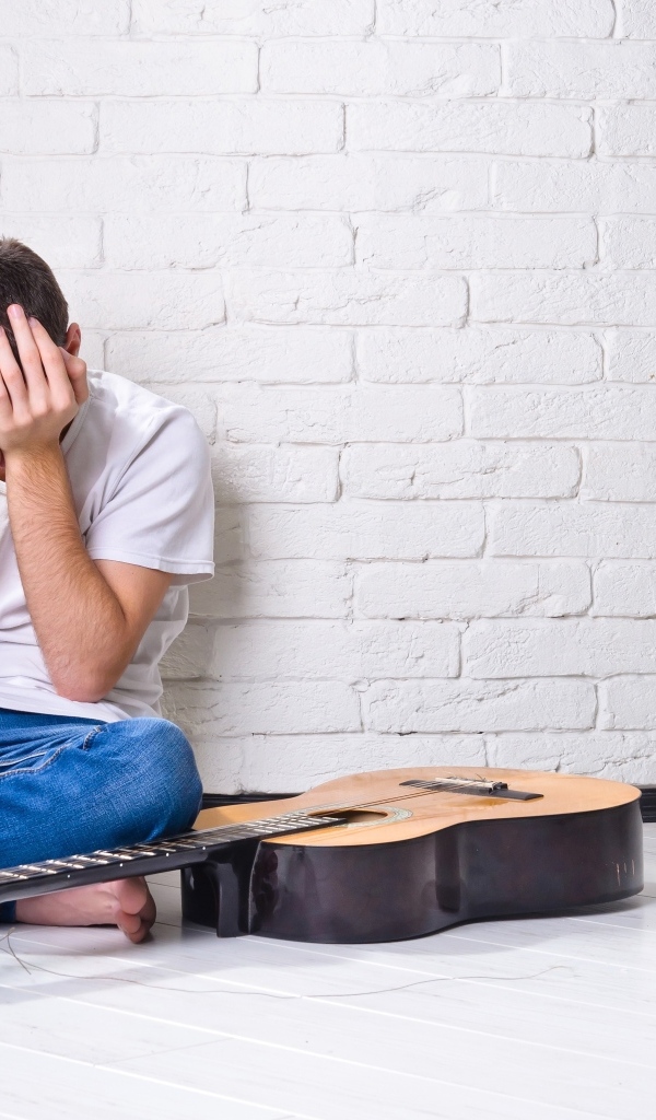 Мужчина с гитарой закрыл лицо руками у стены