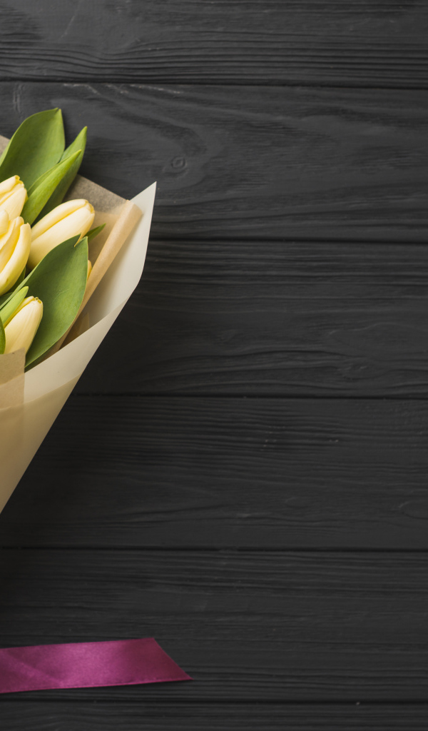 Букет желтых тюльпанов в бумаге на черном столе