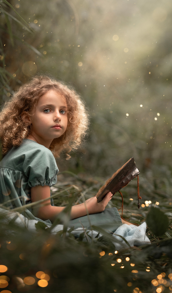 Милая девочка читает книгу сидя на траве