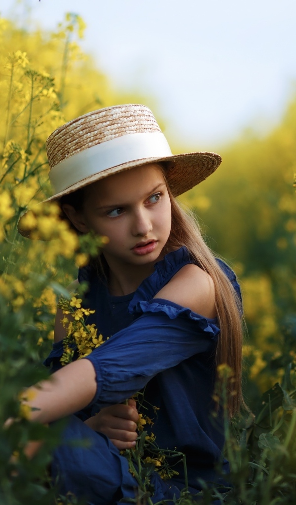 Девочка в шляпе на поле с желтыми цветами рапса