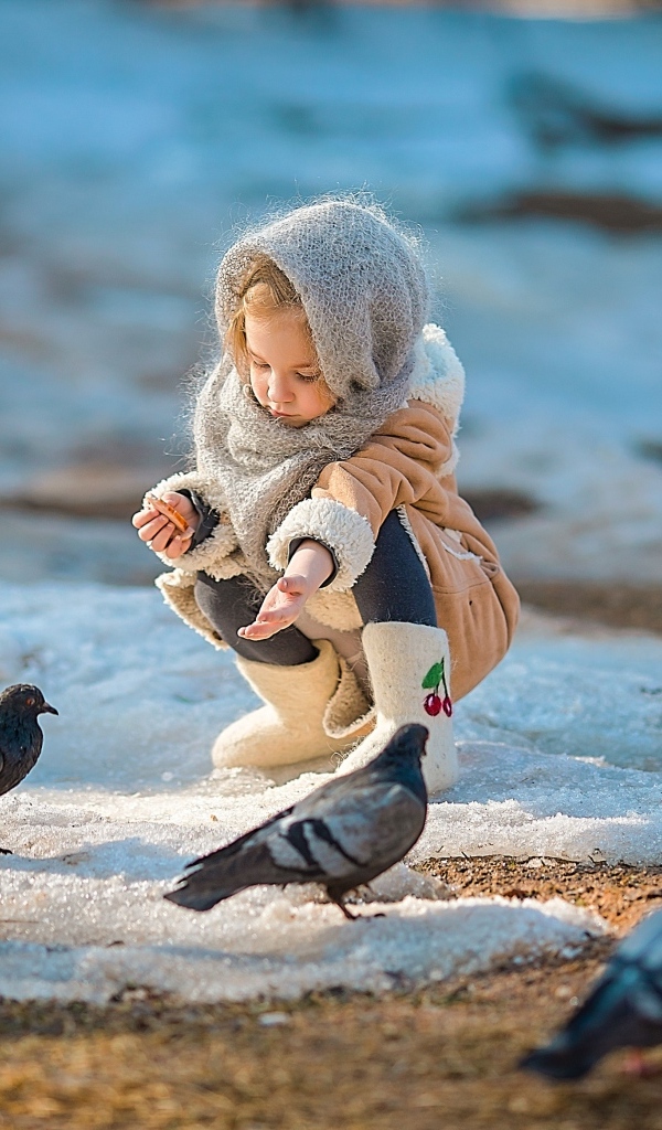 Маленькая девочка кормит голубей зимой