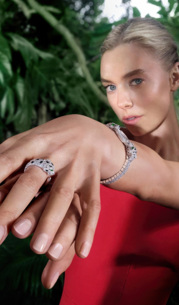 Актриса Ванесса Кирби в красном платье с кольцом на руке на фоне зарослей