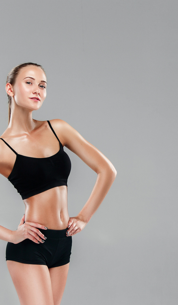 Стройная спортивная девушка в черном наряде на сером фоне