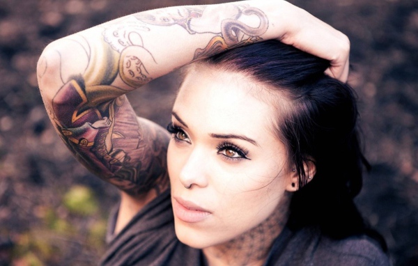 Девушка брюнетка с пирсингом в носу и татуировкой на руке