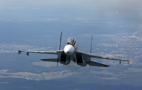 Самолет СУ-27 летит над городом