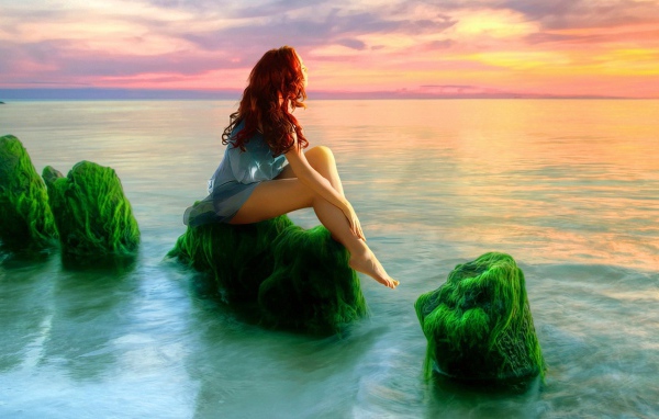Русалка на зеленых камнях смотрит на закат