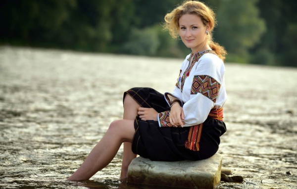Девушка сидит на камне у воды в традиционном наряде