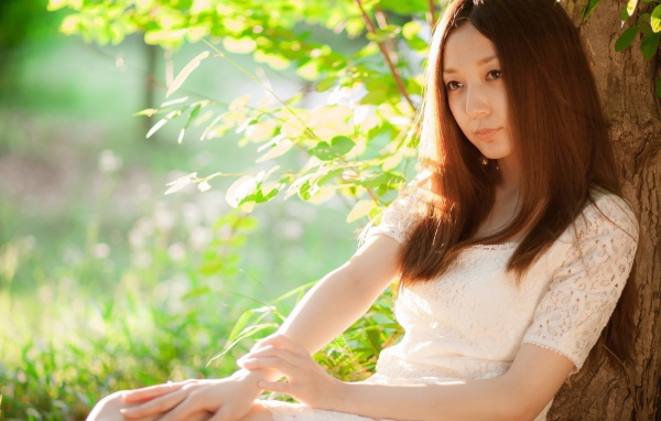 Азиатская девушка прислонилась спиной к дереву
