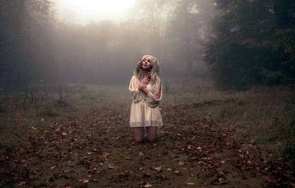 Блондинка в белом платье стоит на коленях среди леса