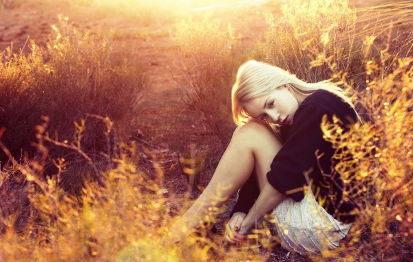 Блондинка сидит среди кустарников