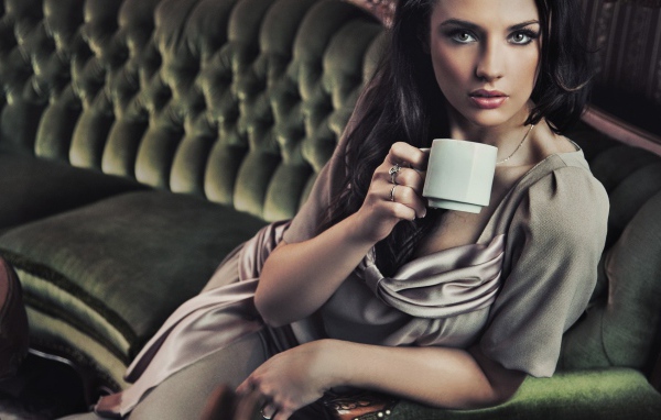 Брюнетка с чашкой кофе сидит на диване