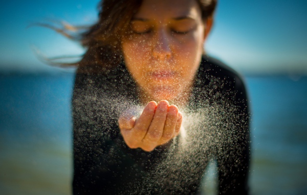 Девушка сдувает песок с руки