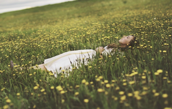 Девушка лежит в поле среди одуванчиков