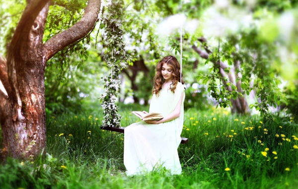 Девушка сидит на качелях и читает книгу