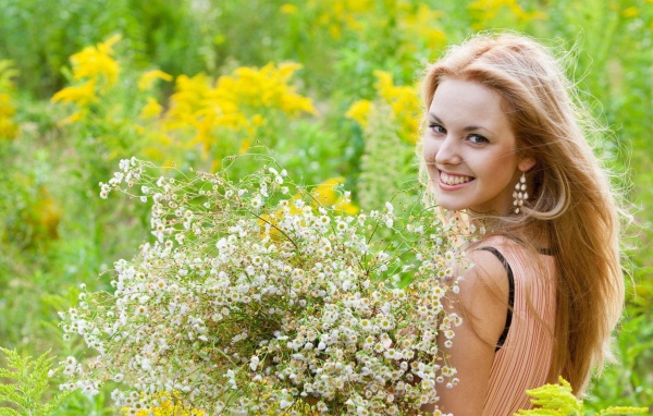 Девушка улыбается, держа в руках букет ромашек