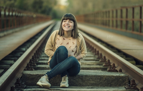 Девушка улыбается сидя на рельсах