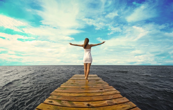 Девушка стоит раскинув руки на краю причала