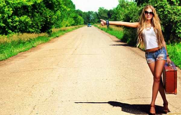 Девушка с чемоданом занимается автостопом