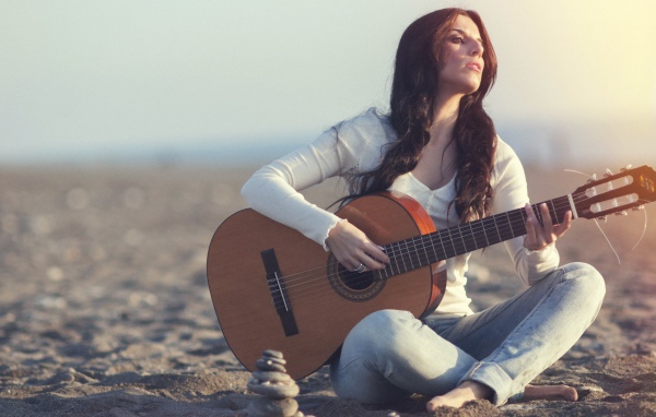 Греческая девушка сидит с гитарой на пляже
