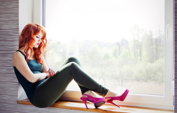 Рыжая девушка в розовых туфлях сидит на окне